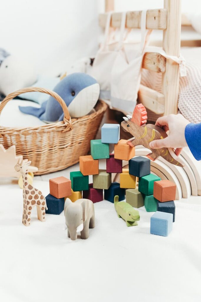 A child's hand arranges colorful wooden toys and animal figures on a playroom floor.